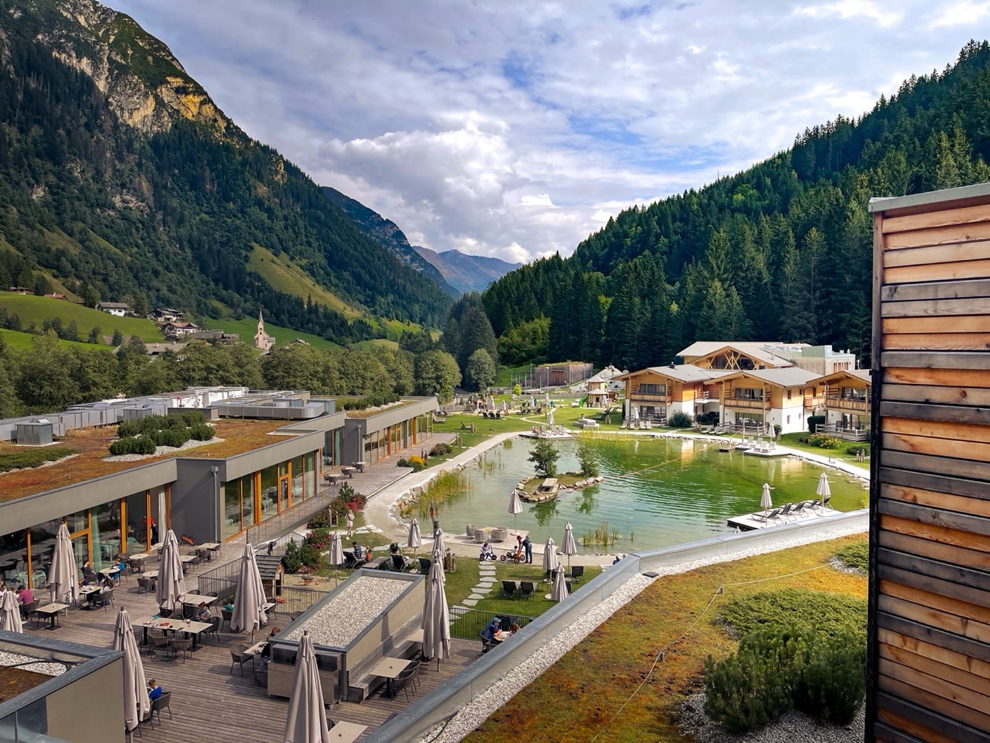 Blick über das Feuerstein in Südtirol: Naturbadesee, Chalets und Terrasse, dahinter das Tal